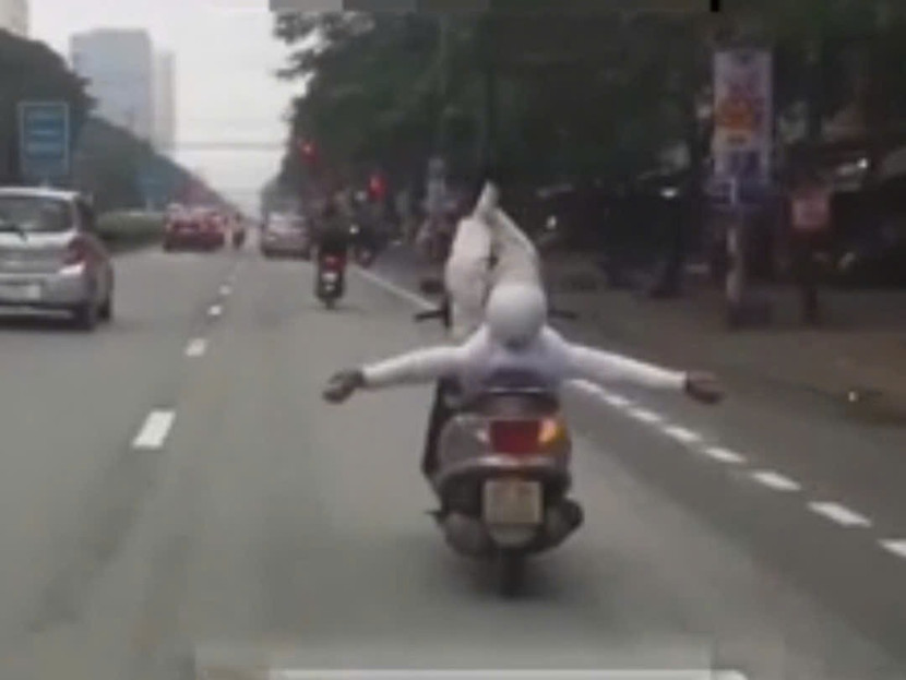 Người đàn ông có hành động nằm ngả, giơ chân lên trời, buông hai tay khi đang điều khiển xe máy. Hình ảnh cắt từ clip