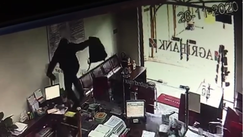 Hình ảnh đối tượng leo qua tấm kính ngăn giữa khách hàng và nhân viên ngân hàng để thực hiện ý đồ cướp tiền (Ảnh: Trích xuất camera)