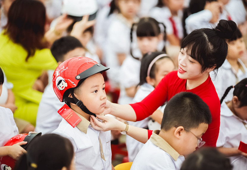 Giáo viên hướng dẫn các em đội mũ bảo hiểm đúng cách