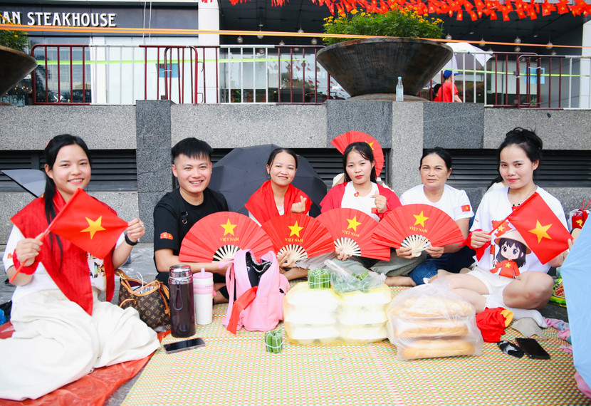 Bà Hiền cùng 13 thành viên đoàn từ Thanh Hóa lên Hà Nội, chờ từ 9h30 để xem diễu binh, mang theo nhiều nhu yếu phẩm, và không thể thiếu là các vật phẩm có in hình cờ đỏ sao vàng, sẵn sàng chào đón các khối diễu binh, diễu hành hợp luyện vào tối cùng ngày