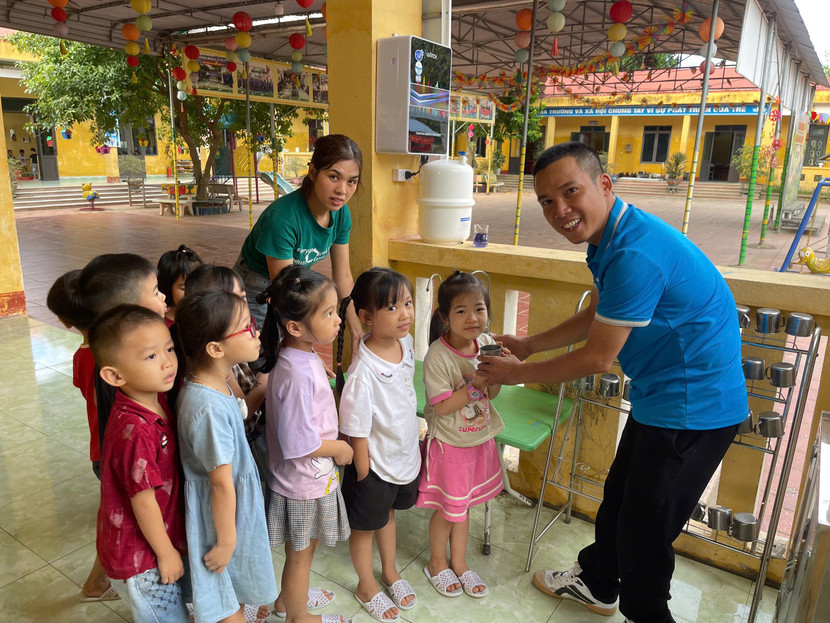 Các em nhỏ háo hức chờ uống nước từ những chiếc máy lọc nước được lắp đặt ngay ngoài lớp học.