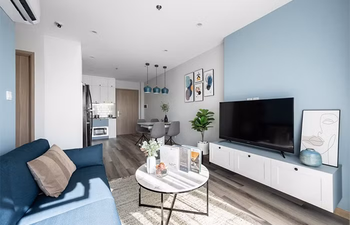 Phòng khách đón ánh sáng tuyệt đẹp từ logia căn hộ, thiết kế vuông vức với một sofa dài, bàn tròn, kệ tivi đơn giản và hiện đại.