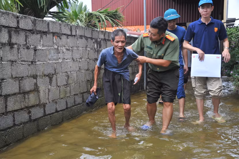 Trung tá Chu Quốc Dũng, Phó Trưởng Ban Biên tập An ninh Thủ đô trò chuyện và giúp ông ông Mai Thế Ba (67 tuổi) ở xóm 2, thôn Khôn Duy, xã Mỹ Lương đi qua chỗ ngập