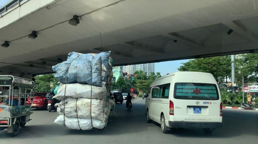 Hai chiếc xe ba bánh trong đó có một xe chất hàng chục bao hàng cồng kềnh trên phố
