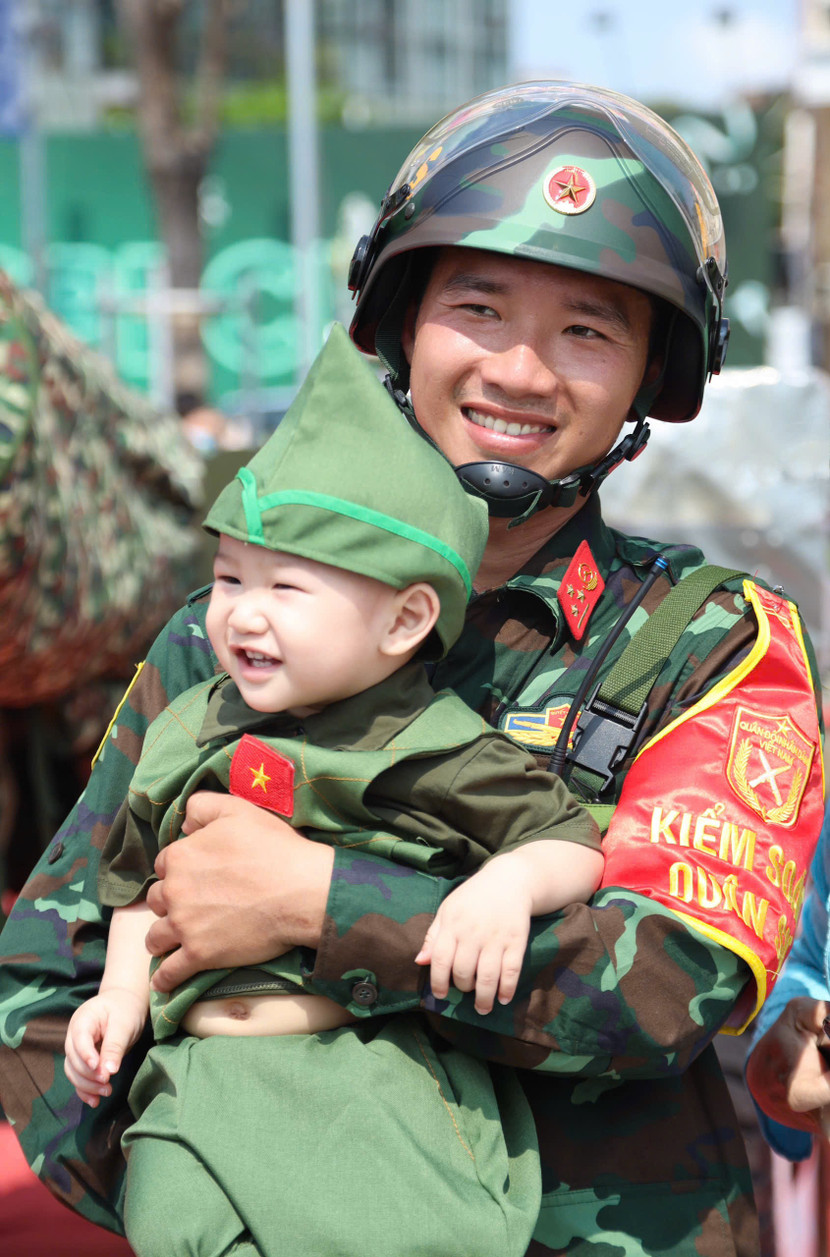 Một em nhỏ trong trang phục Bộ đội Cụ Hồ chụp ảnh cùng chiến sĩ bảo vệ khu vực pháo lễ tại công viên bến Bạch Đằng (Ảnh: DIỄM HẰNG)