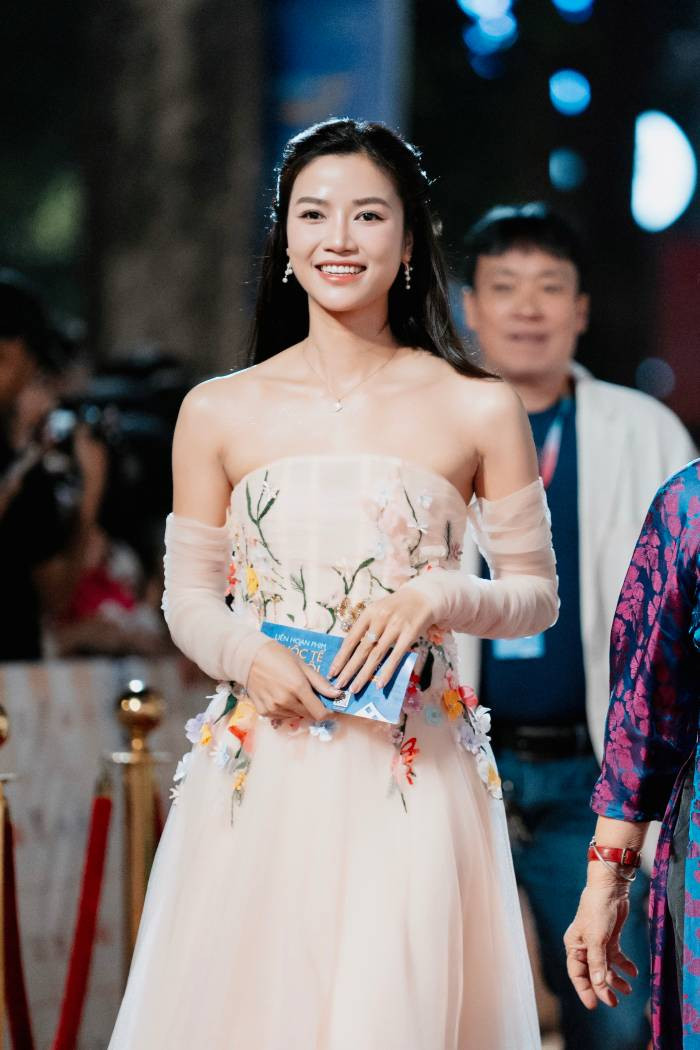 Diễn viên Anh Đào chọn trang phục váy công chúa cúp ngực ngang. Chiếc váy được dựng phom dạng corset cổ điển, phủ vải voan màu hồng da nhẹ nhàng. Trên thân váy đính kết những dải hoa nhiều màu sắc dọc phần eo