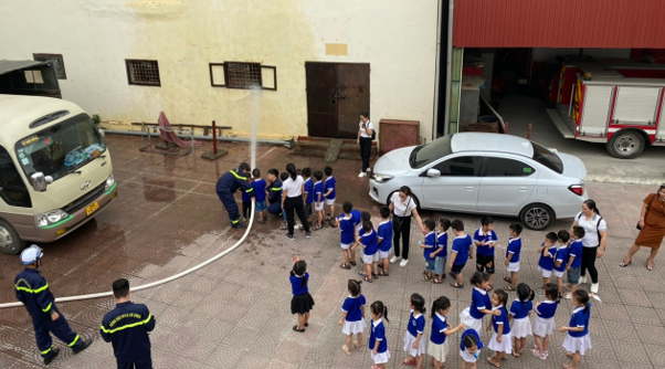 Giáo viên và các em học sinh trải nghiệm cách cầm lăng vòi và phun nước vào đám cháy.