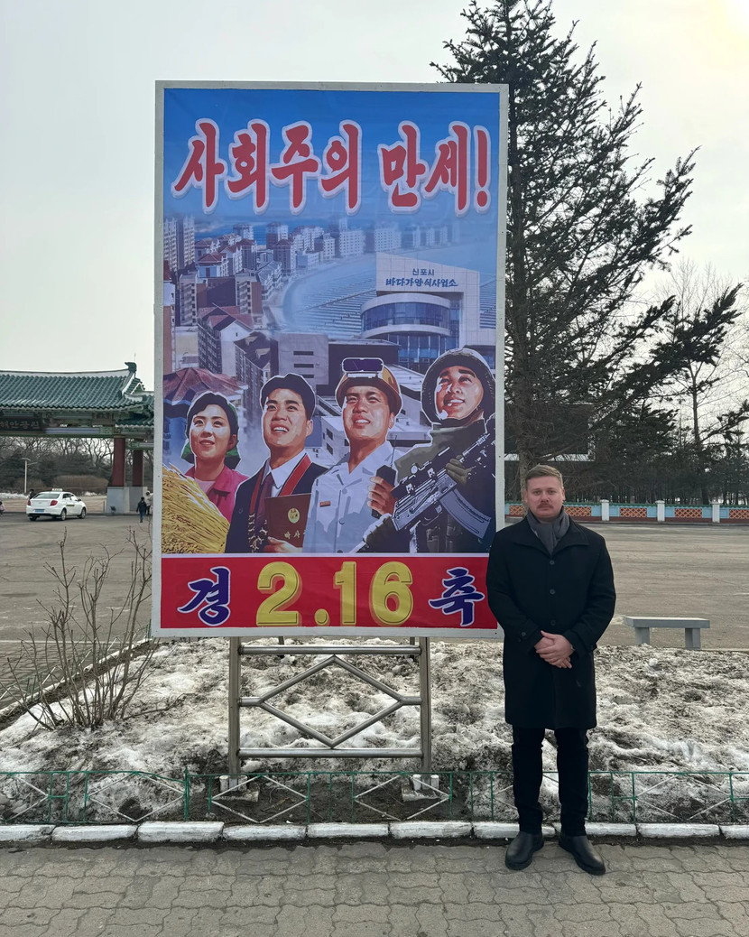 Martell đứng trước tấm biển ở Rason vào ngày 16-2-2025. Dòng chữ có nghĩa: “Chủ nghĩa xã hội muôn năm!”