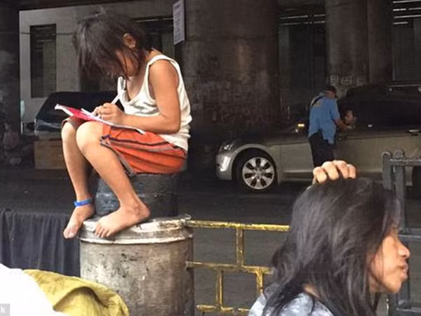 Bé gái mải mê học tập cạnh con đường đông đúc ảnh 1