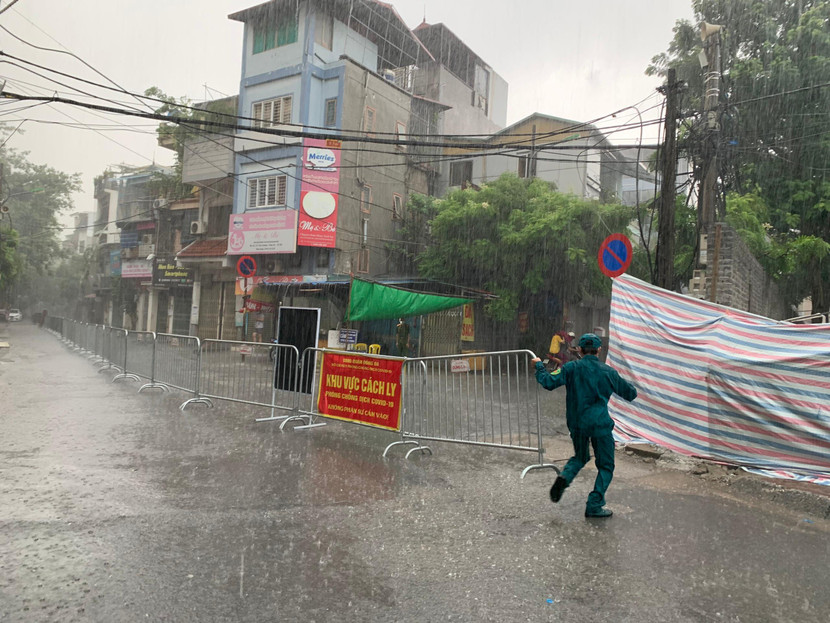 Một cán bộ dân phòng lao mình dưới màn mưa để sắp xếp lại barie phong tỏa ngay ngắn, đúng vị trí quy định