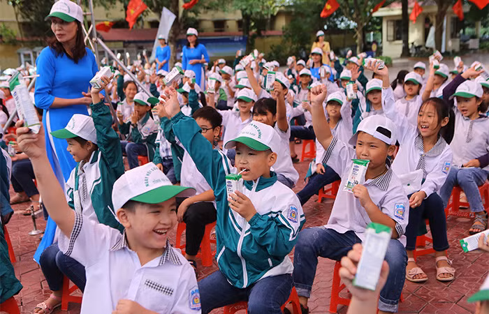 Các em học sinh Trường tiểu học A hào hứng tham gia hoạt động uống sữa cùng các bạn tại sân trường trong buổi lễ phát động